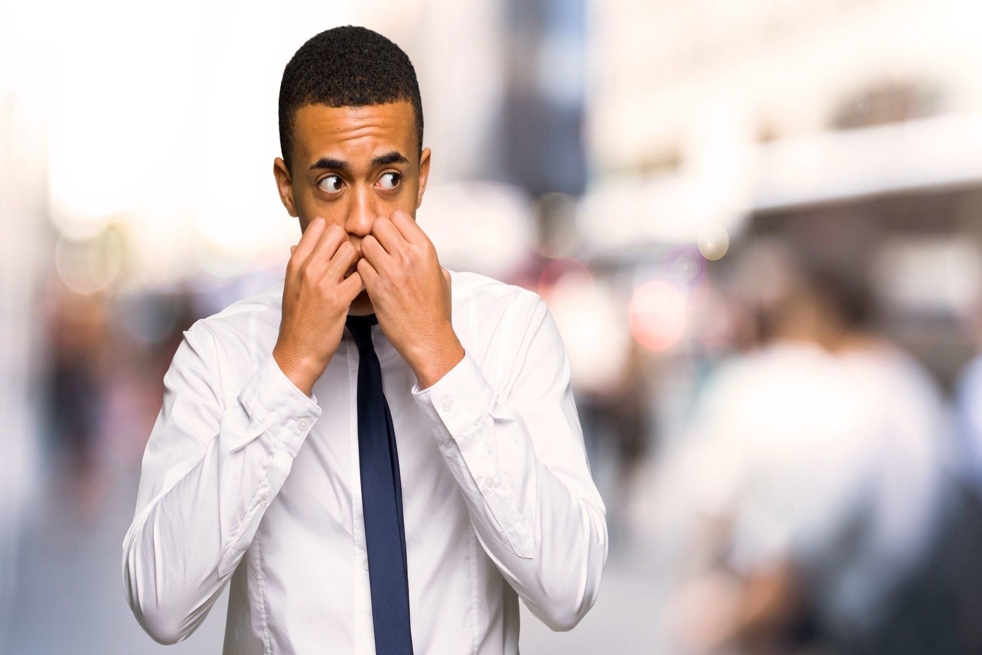 Young afro american businessman is a little bit nervous and scared putting hands to mouth